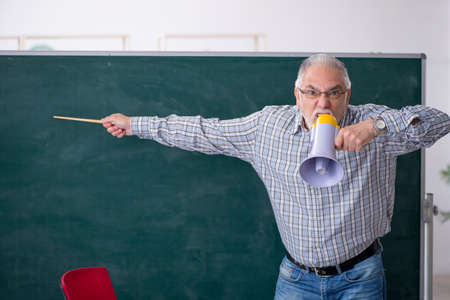 Old male teacher holding megaphone in the classroomの写真素材