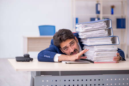 Young male employee and too much work in the officeの写真素材
