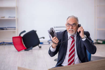 Old male employee working overtime in the officeの写真素材