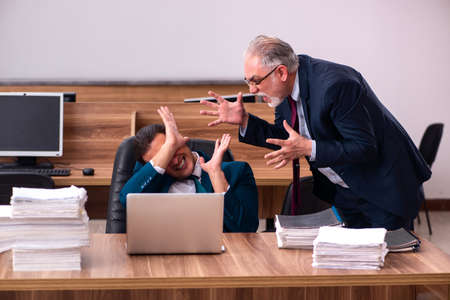 Old male employer and young male assistant in bullying conceptの写真素材