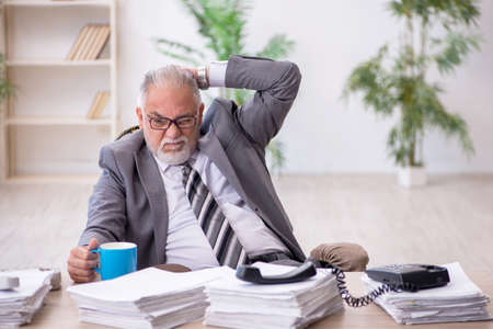 Old male employee and too much work in the officeの写真素材