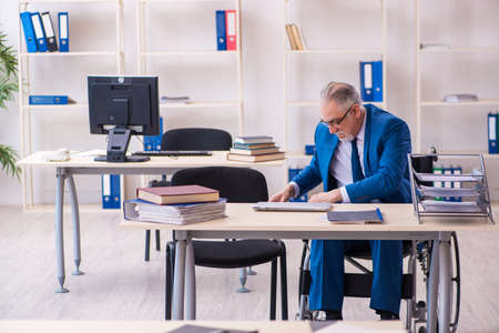 Old male employee in wheel-chair sitting in the officeの写真素材