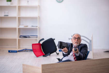 Old male employee working overtime in the officeの写真素材