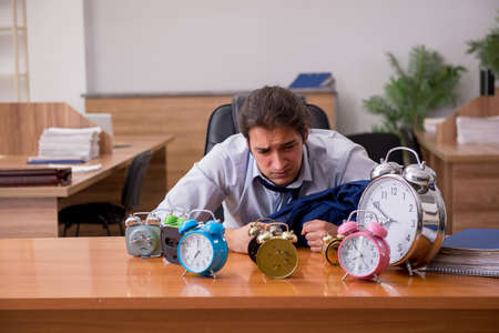 Young male employee sleeping in the office in time management coの写真素材