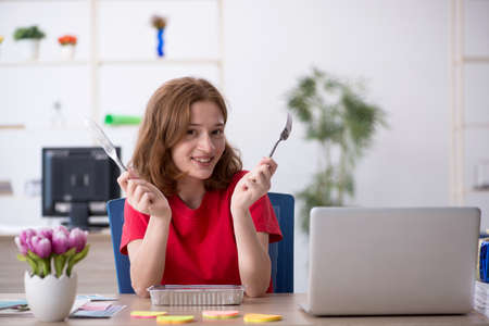 Young female designer having breakfast in the officeの写真素材