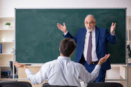 Old male teacher and young male student in front of green boardの写真素材