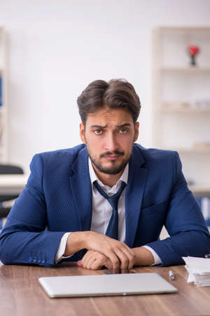 Young male employee unhappy with excessive work in the officeの写真素材