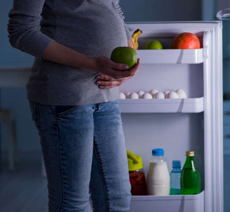 Pregnant woman near fridge looking for food and snacks at night