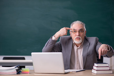 Old male teacher in front of blackboardの写真素材