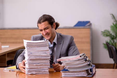 Young male employee and too much work in the officeの写真素材