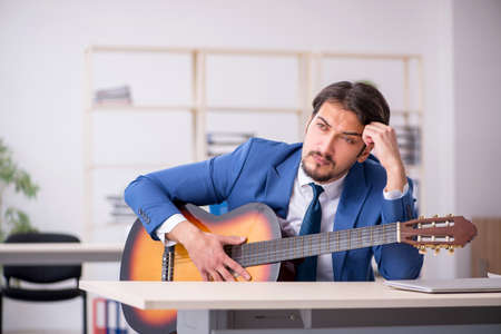 Young male employee playing guitar at workplaceの写真素材