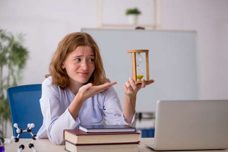 Young female chemist student in time management concept