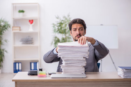 Young male employee and too much work in the officeの写真素材