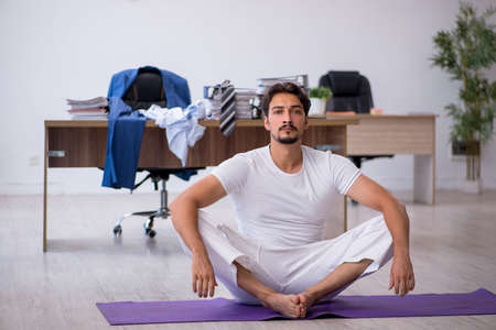 Young male employee doing sport exercises in the officeの写真素材