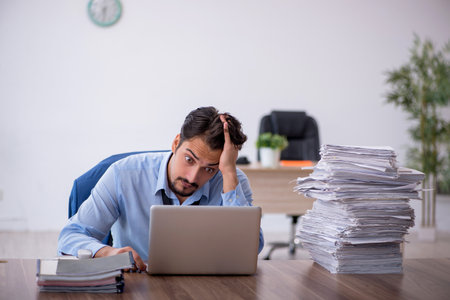 Young male employee unhappy with excessive work in the officeの写真素材