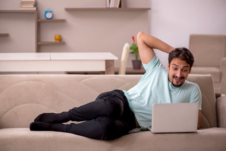 Young man sitting on the sofa with computer at homeの写真素材