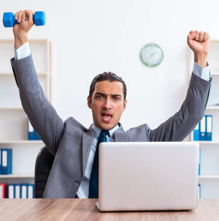 Young handsome employee doing sport exercises at workplaceの写真素材