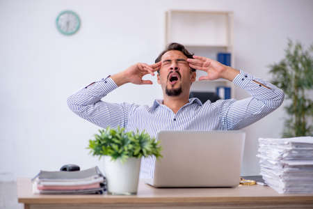 Young male employee unhappy with excessive work in the officeの写真素材