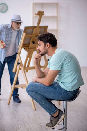 Old painter and young male model at the studioの写真素材