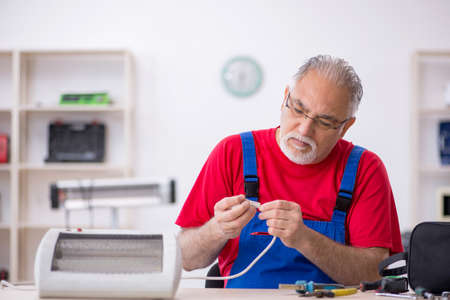 Old repairman repairing heater at workshopの写真素材