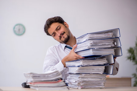 Young male employee and too much work in the officeの写真素材