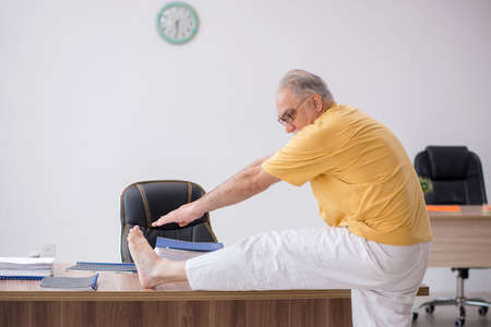 Old businessman employee doing sport exercises in the officeの写真素材