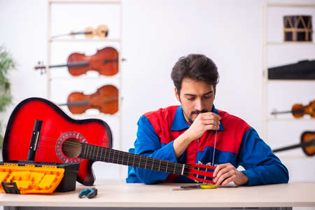 Young male repairman repairing musical instruments at workplaceの写真素材