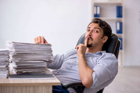 Young male employee unhappy with excessive work in the officeの写真素材