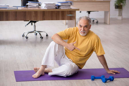 Old businessman employee doing sport exercises in the officeの写真素材