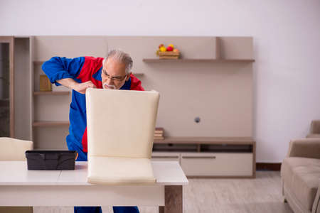 Old male carpenter repairing chair indoorsの写真素材
