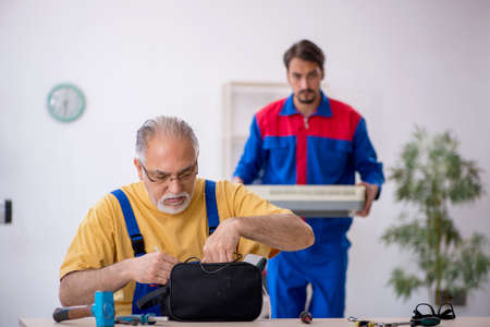 Two male repairmen repairing air-conditioner
