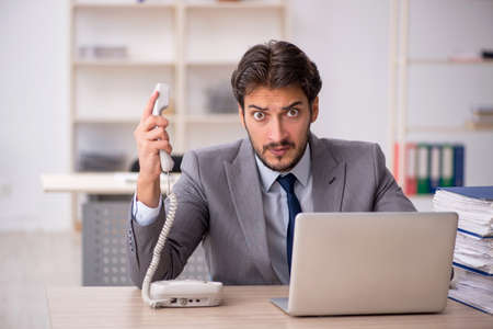 Young male employee and too much work in the officeの写真素材