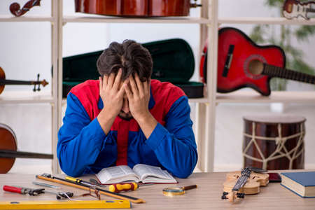 Young man repairing musical instruments at workshopの写真素材