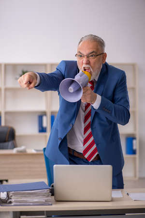Angry old businessman holding megaphone in the officeの写真素材