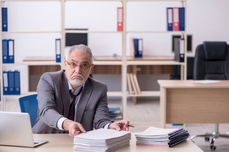 Old male employee unhappy with excessive work in the officeの写真素材