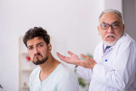 Young male patient with hearing problem visiting old doctor otorの写真素材