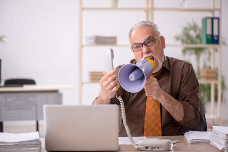 Angry boss employee holding megaphone at workplaceの写真素材