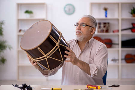Old male repairman repairing musical instruments at workshop