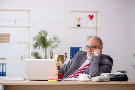 Old male employee being awarded with golden cupの写真素材