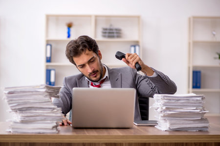 Young male employee unhappy with excessive work in the officeの写真素材