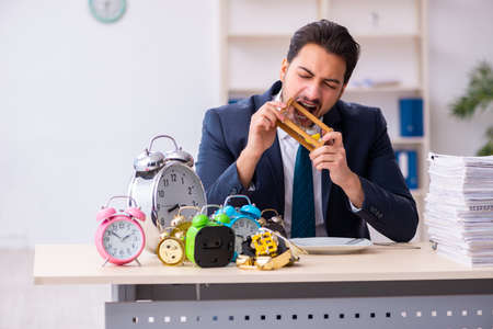 Young businessman employee eating alarm-clockの写真素材