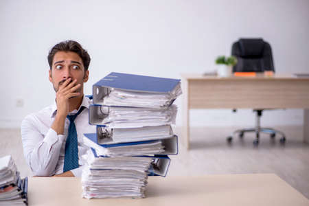 Young male employee and too much work in the officeの写真素材