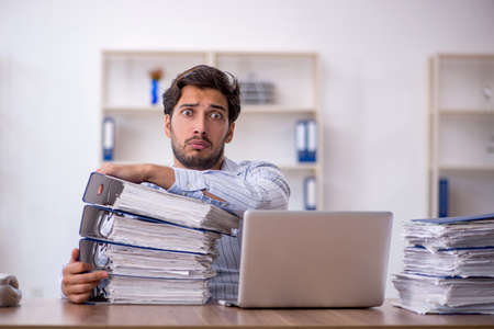 Young male employee unhappy with excessive work in the officeの写真素材