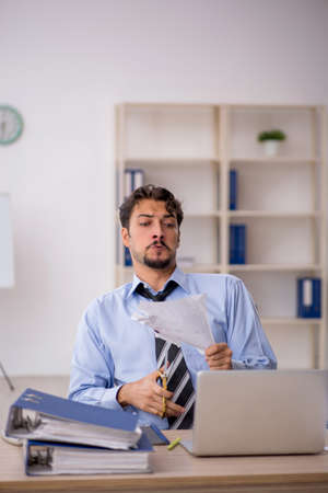 Young male employee unhappy with excessive work in the officeの写真素材