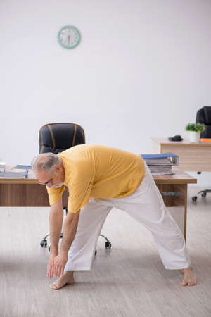 Old businessman employee doing sport exercises in the officeの写真素材