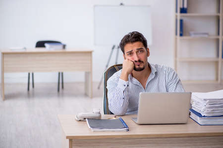 Young male employee and too much work in the officeの写真素材