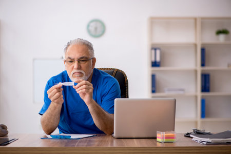 Old male doctor holding thermometer in the clinicの写真素材