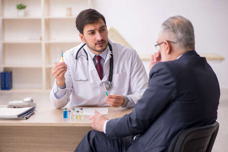 Old businessman visiting young male doctor in vaccination concepの写真素材