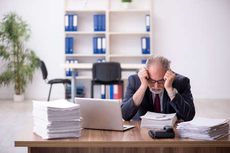 Old male employee and too much work in the officeの写真素材