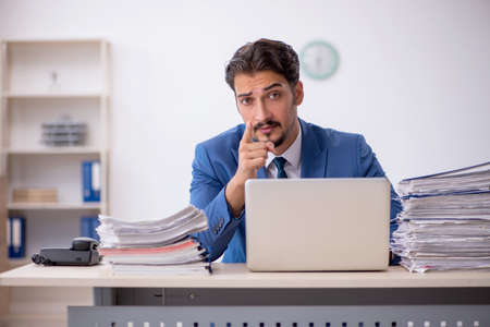 Young male employee and too much work in the officeの写真素材